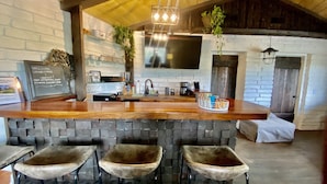 A bar area with a wooden counter, a large TV screen, and three bar stools. - Tranquil country setting w/majestic views (Escondido)