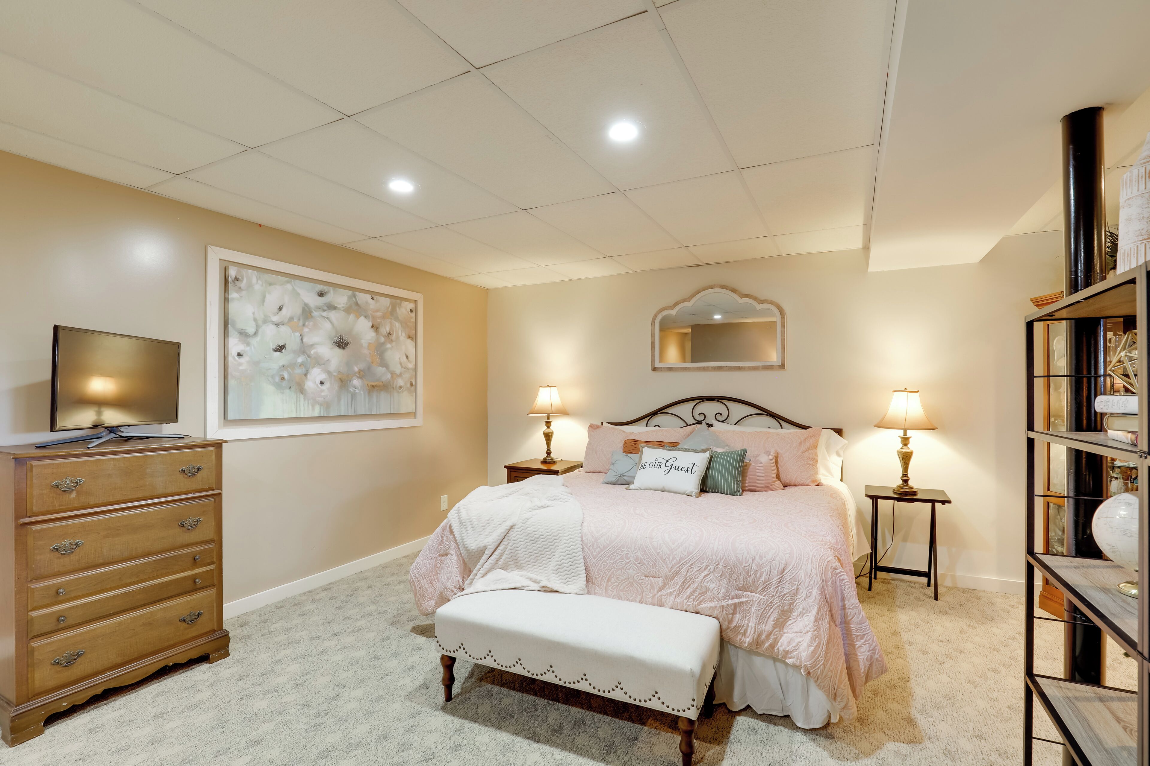 A bedroom with a bed, dresser, bench, and a TV on a stand.