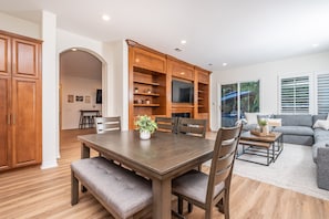 A dining area with a wooden table and benches, a kitchen with wooden cabinets, and a living room with a sofa and a TV. - Luxury Retreat-Pool/HotTub/Game Room/Putting Green (Escondido)