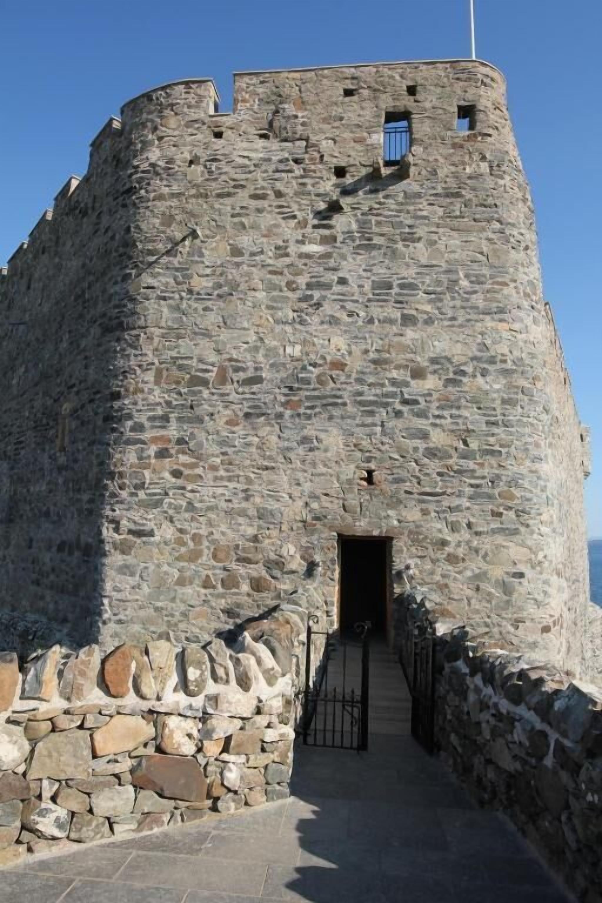 Ein steiner Turm mit schmalem Eingang und einer Fahnenstange.