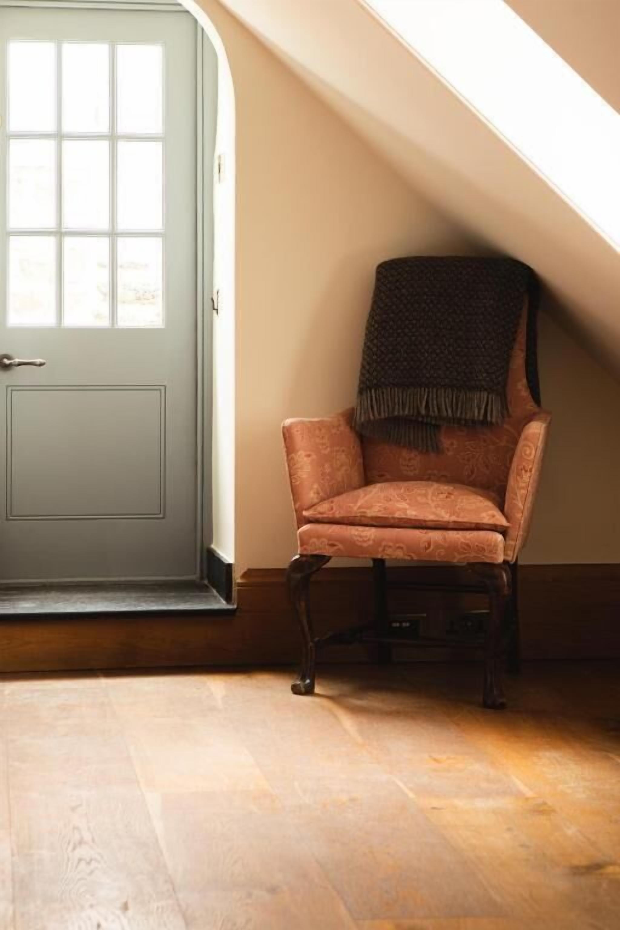 A room with a wooden floor, a light blue door, and a patterned armchair with a throw blanket.