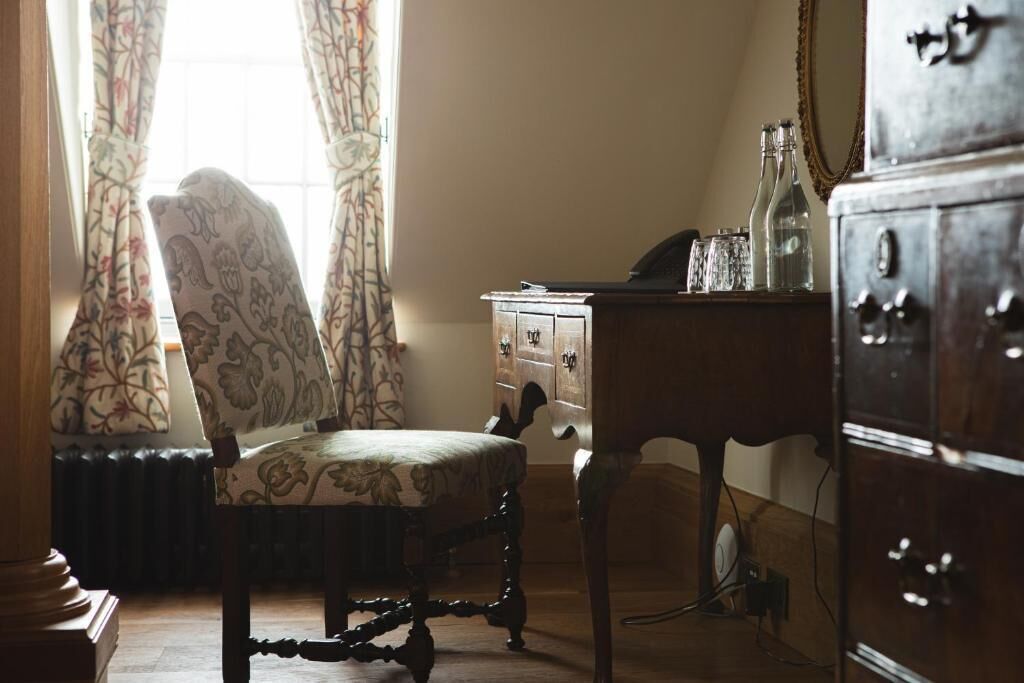 A room with a vintage chair, a wooden dresser, and a small table with bottles.