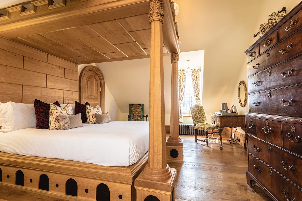 A spacious bedroom with a large wooden four-poster bed, a wooden dresser, and a classic chair.