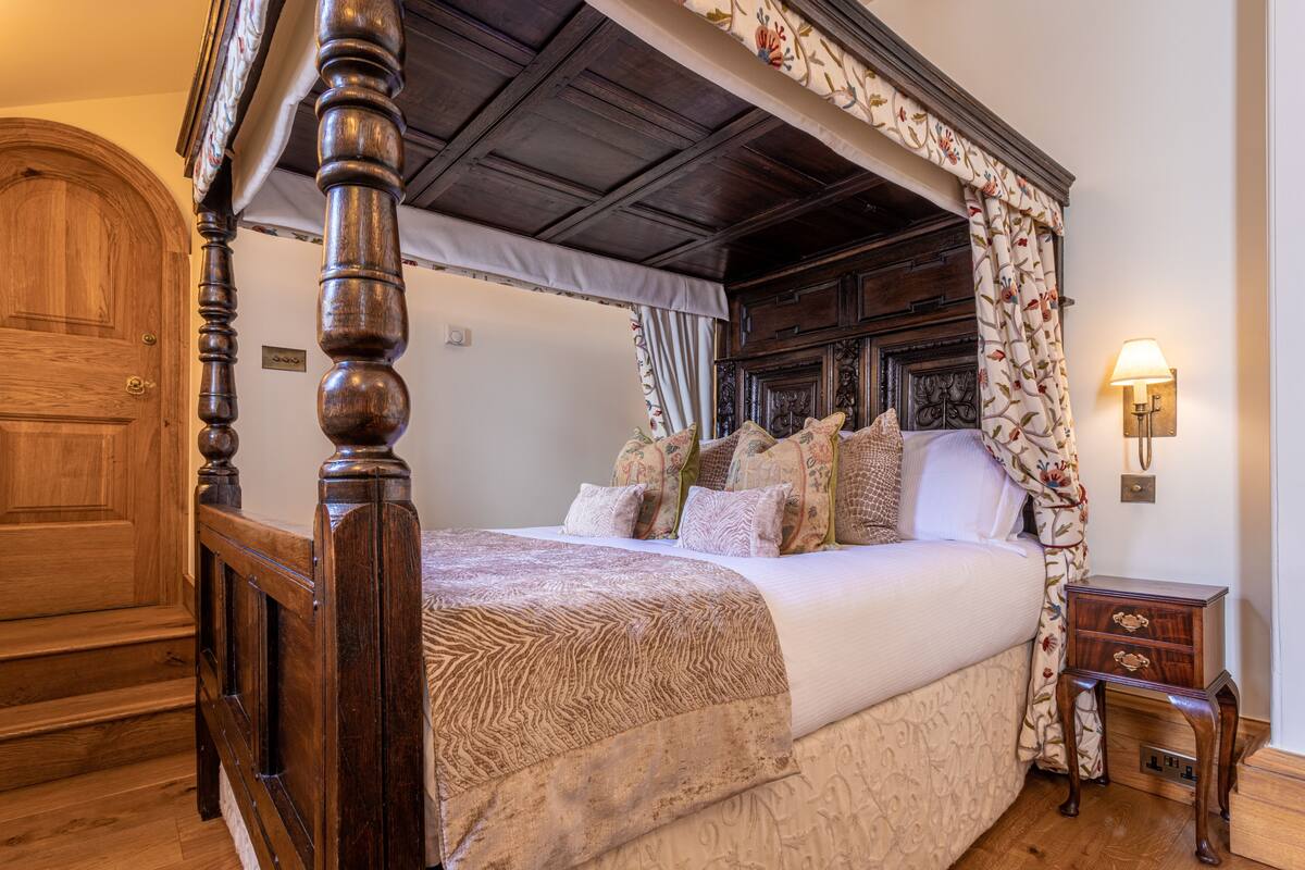 A four-poster bed with a canopy, a wooden nightstand, and a wall-mounted lamp.