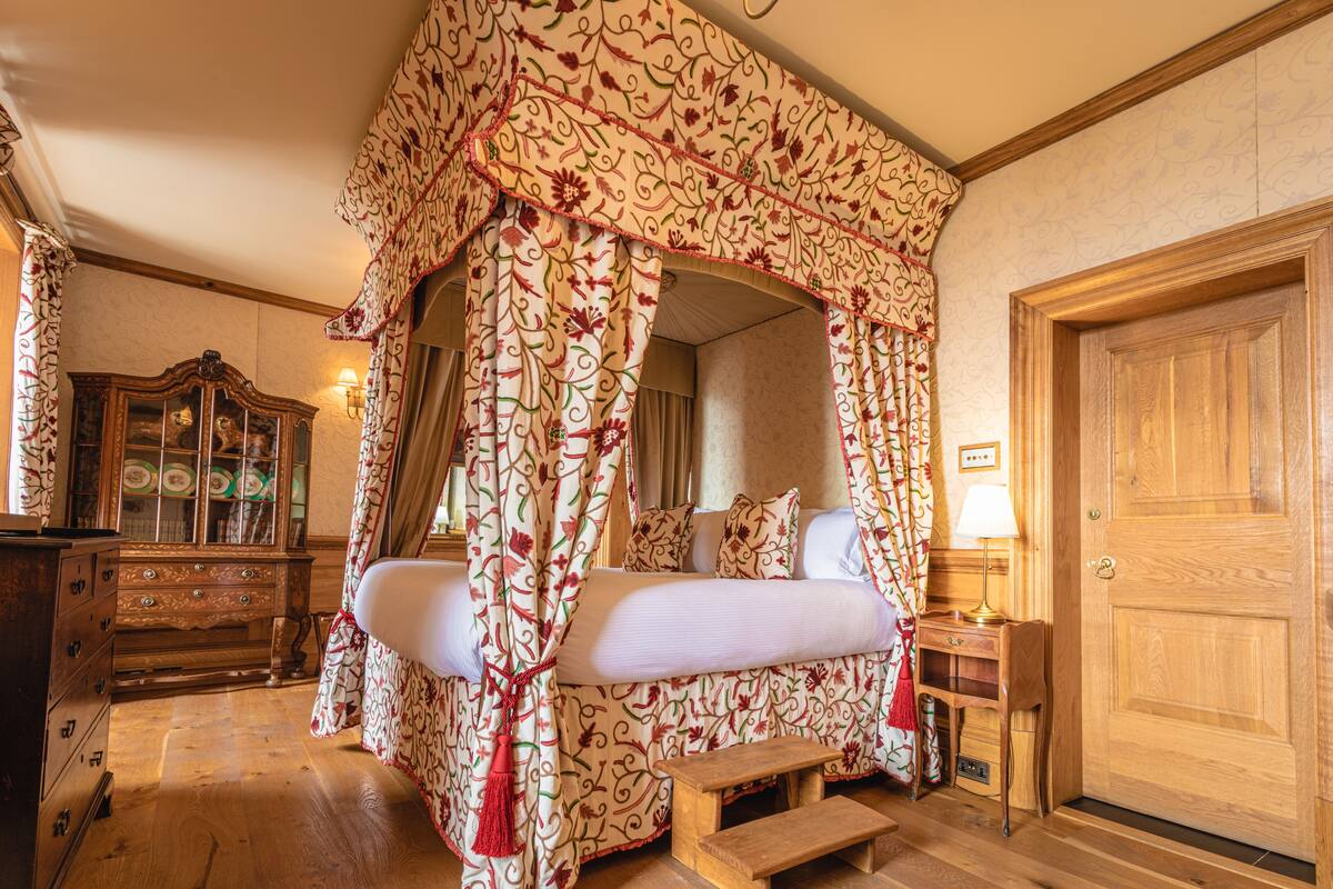 A bedroom with a canopy bed, wooden furniture, a mirror, and a door.