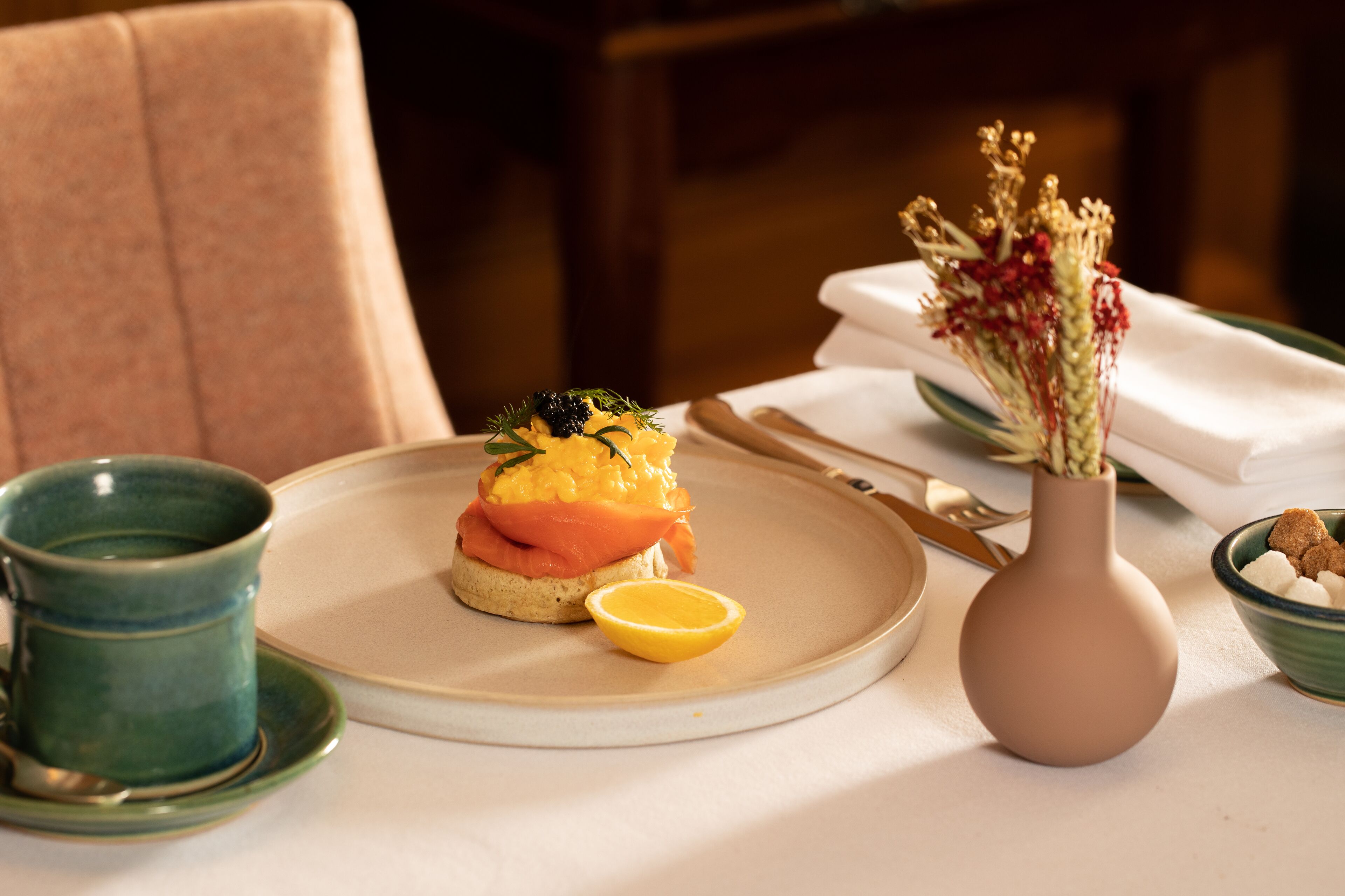 A plate with a salmon sandwich, a lemon wedge, and a small bowl of nuts.