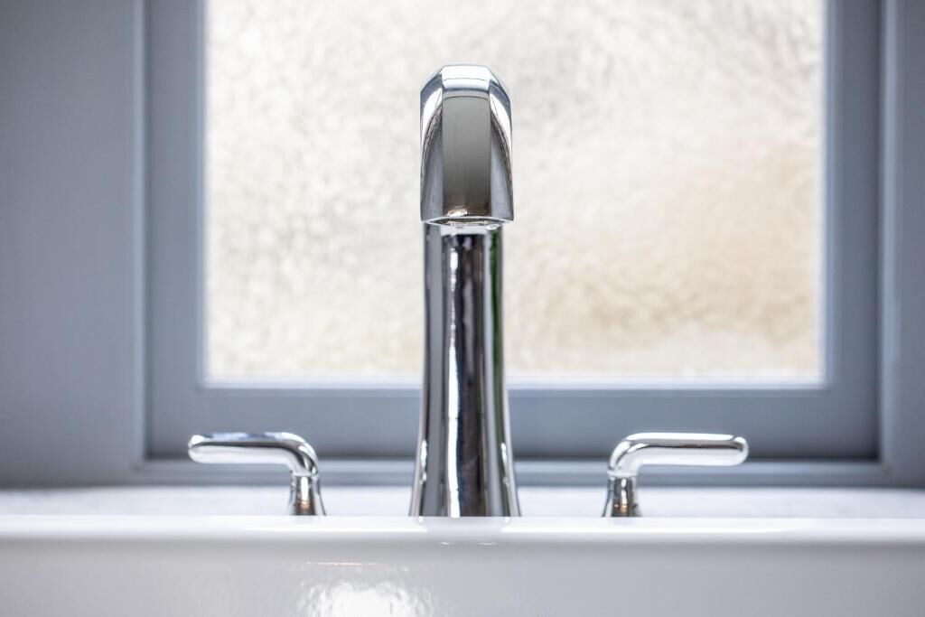 Un lavabo de salle de bain avec un robinet chromé et une fenêtre en arrière-plan.