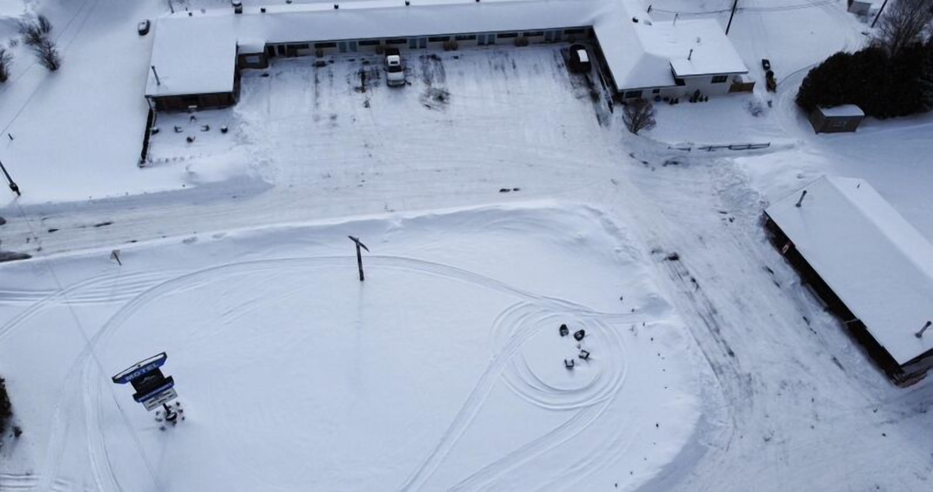 Vista aérea de un estacionamiento cubierto de nieve con algunos vehículos y una quitanieves.