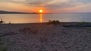 Una playa con un atardecer sobre el agua, un bote a la izquierda y una costa distante.