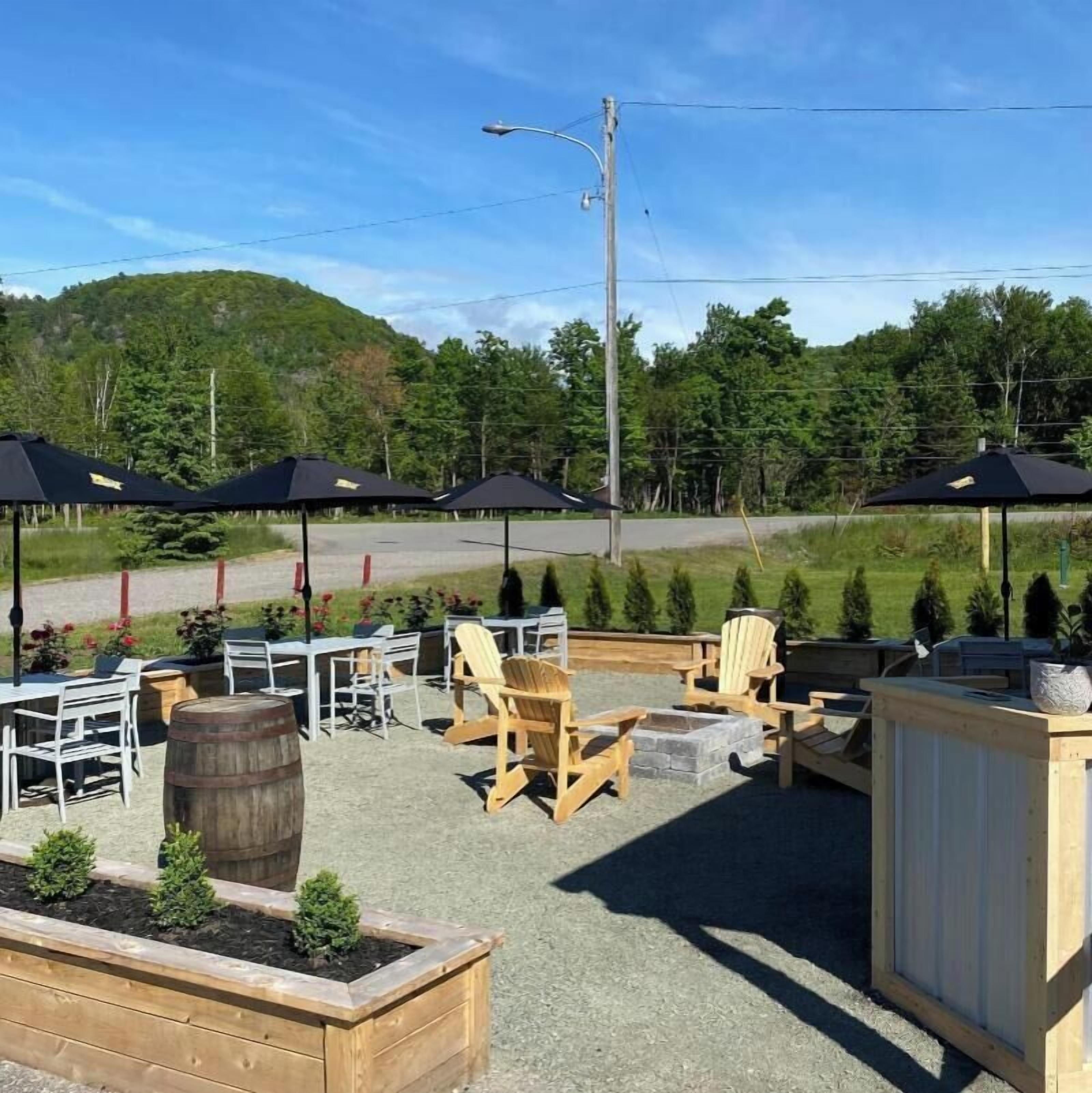 An outdoor seating area with wooden chairs and tables, surrounded by planters and umbrellas.
