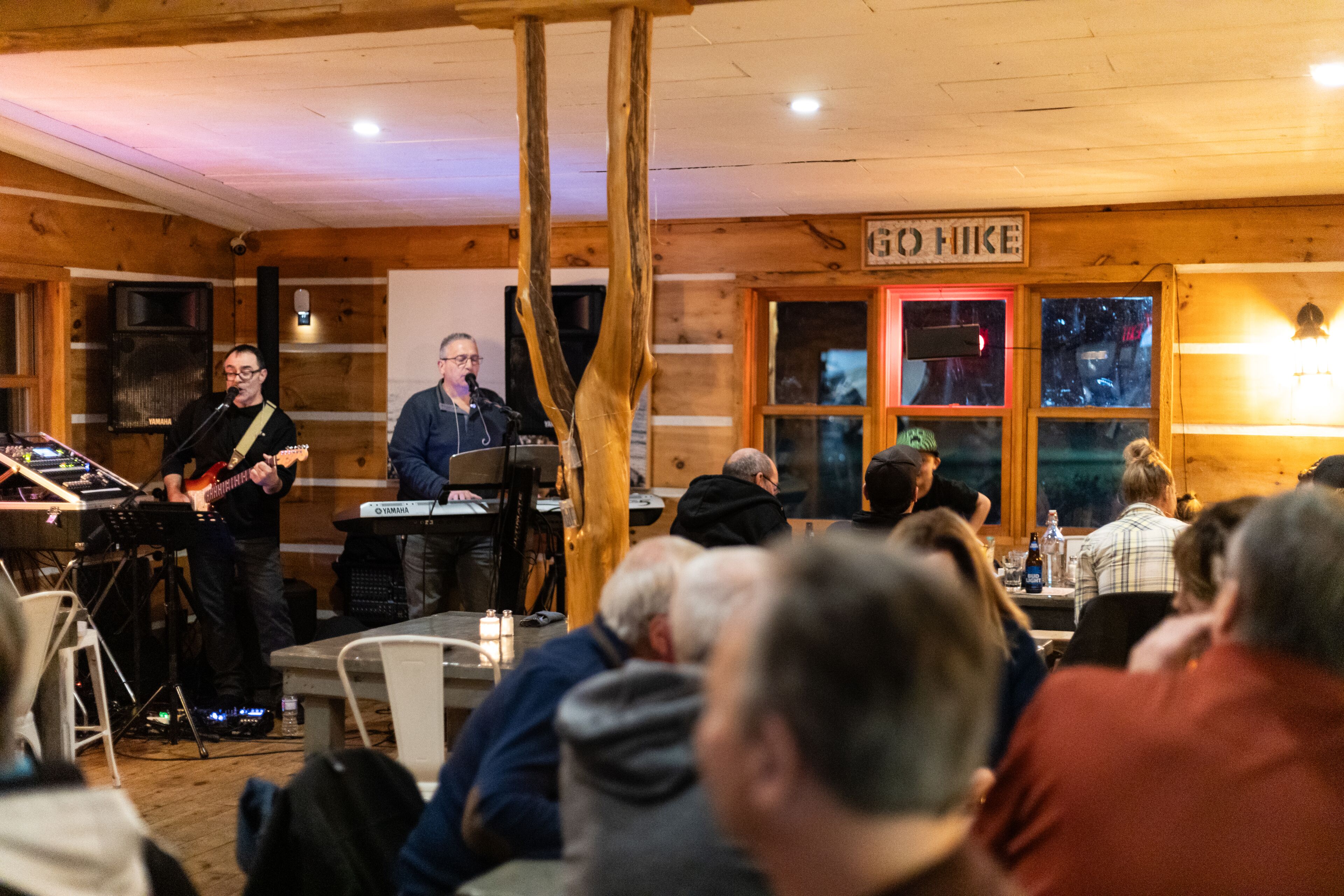A wooden interior with a stage for live music, tables for dining, and a sign that reads "GO HIKING".