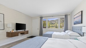 Habitación de hotel moderna con una cama grande, televisor, escritorio y ventana con vistas a la montaña.