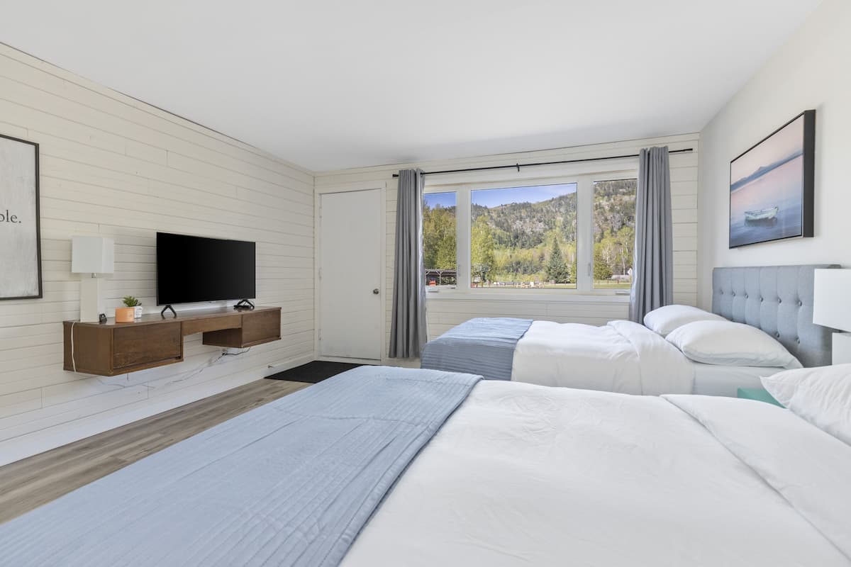 A modern hotel room with a large bed, a TV, a desk, and a window with a mountain view.