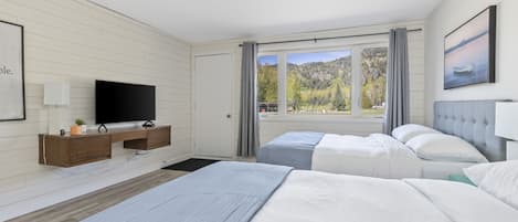 A modern hotel room with a large bed, a TV, a desk, and a window with a mountain view.