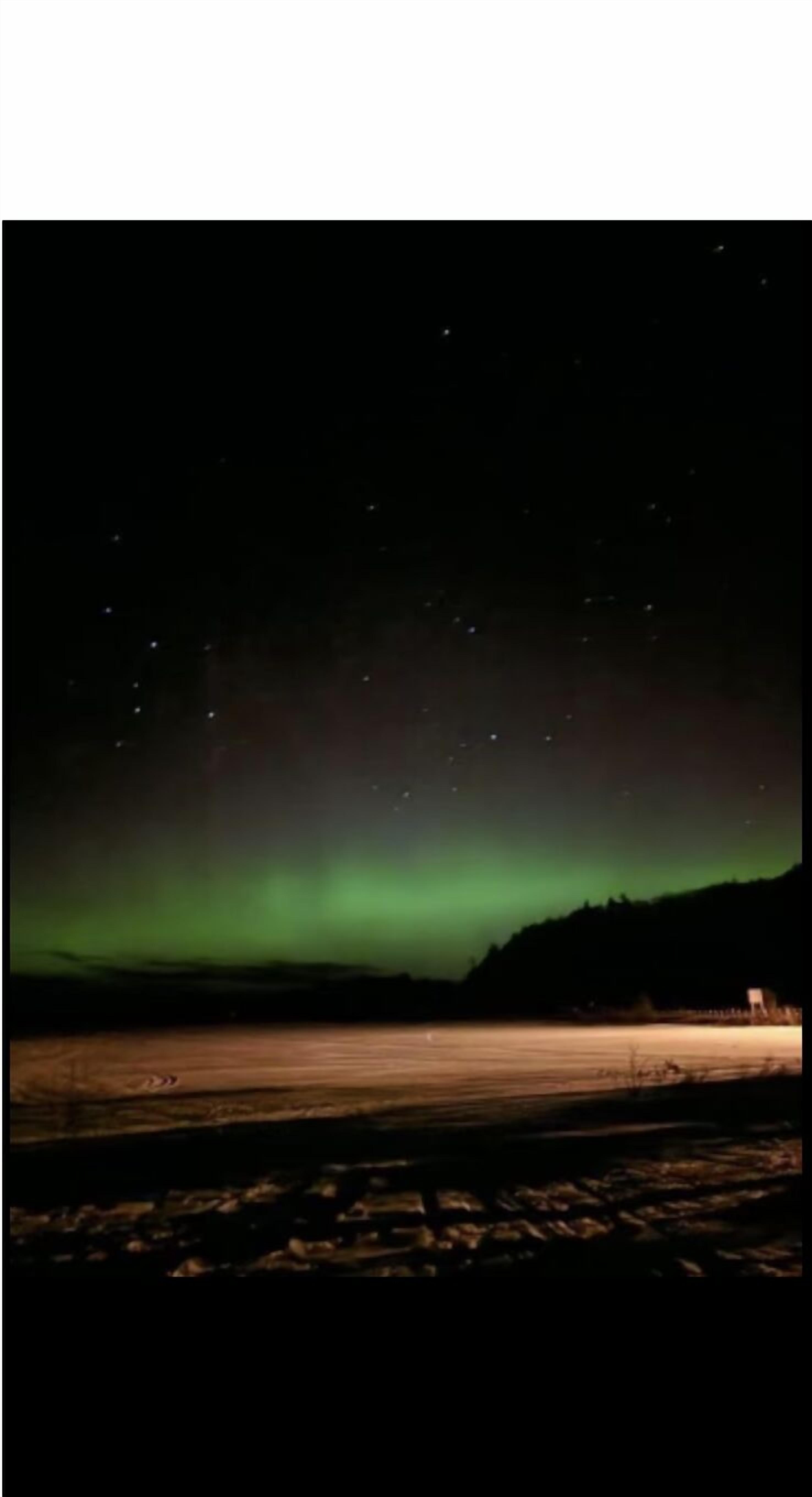 Cielo nocturno con estrellas visibles y la aurora boreal.