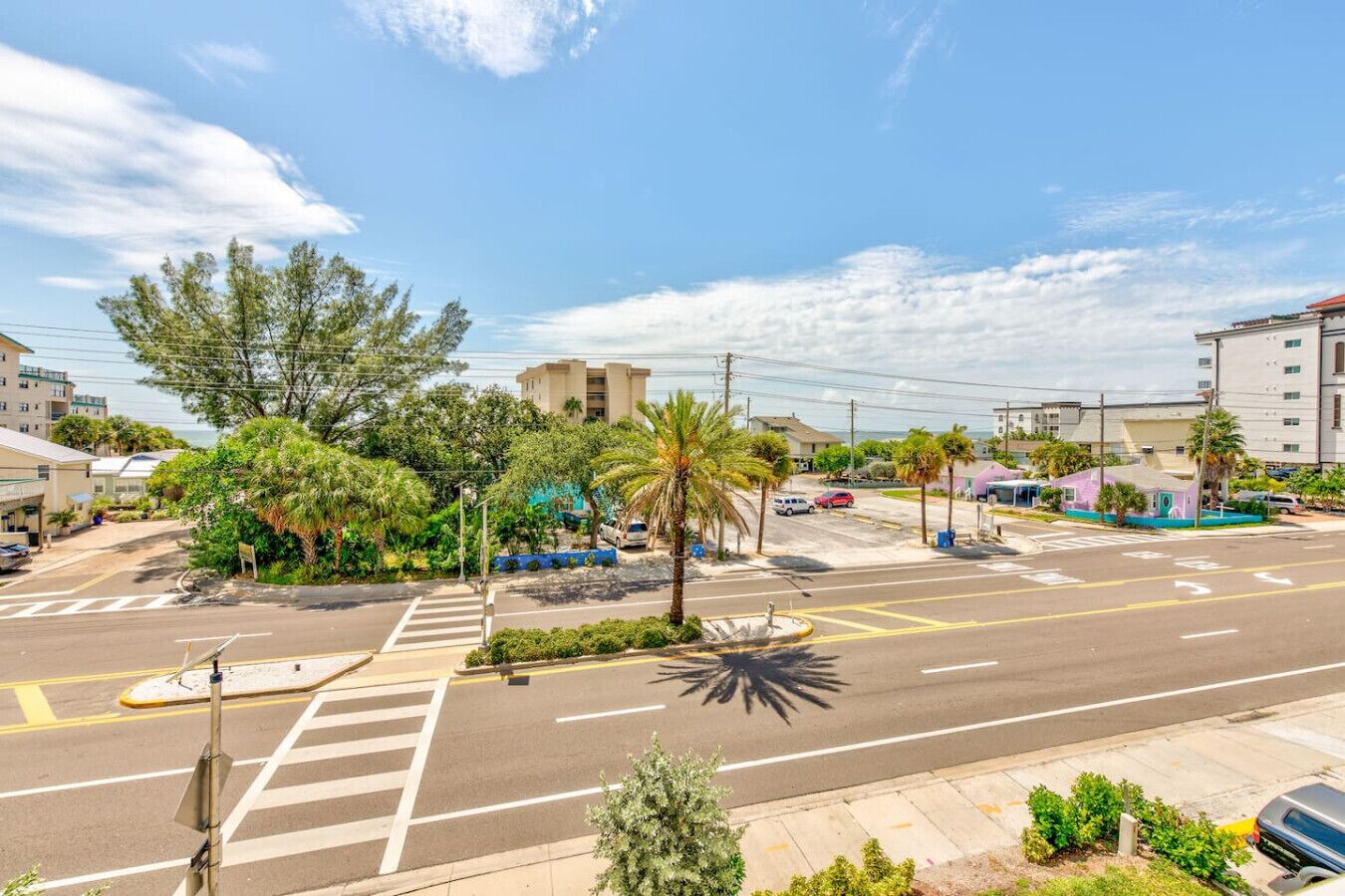 A street view with a crosswalk, palm trees, and buildings.