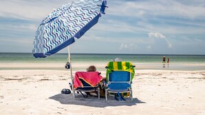 Zwei Strandstühle mit Handtüchern, ein Strandsonnenschirm und ein sandiger Strand.