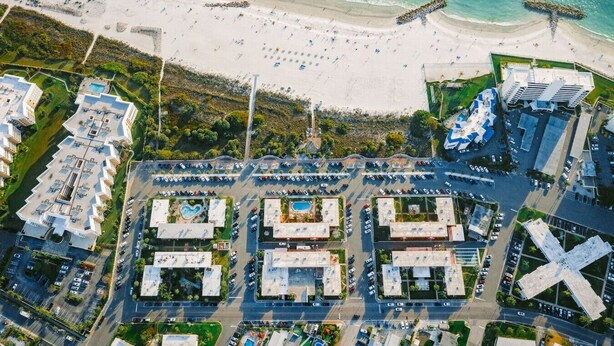 Luftaufnahme einer Küstenregion mit Strand, Parkplatz und modernen Gebäuden.