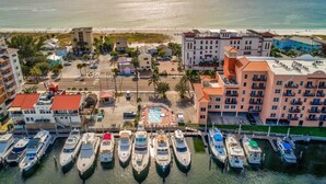 A marina with multiple boats docked, a central pool, and surrounding buildings with balconies. - Lovely Water View Condo | Top Floor | Steps to Beach (Madeira Beach)