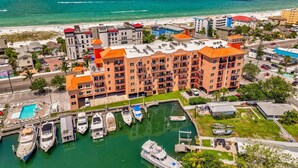 A multi-story hotel with balconies, a marina with boats, and a beach in the background. - Lovely Water View Condo | Top Floor | Steps to Beach (Madeira Beach)