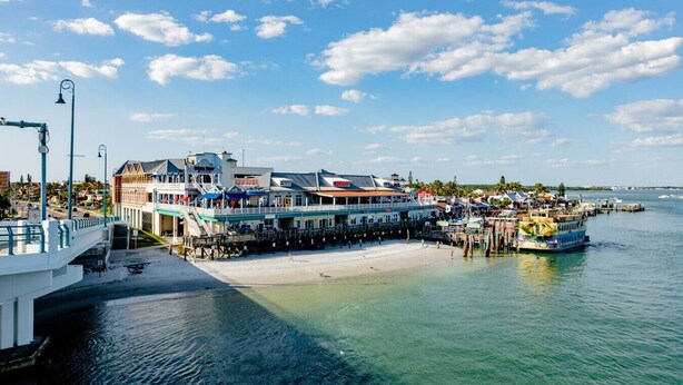 A waterfront hotel with a pier extending into the water, a beach, and a view of the ocean. - Lovely Water View Condo | Top Floor | Steps to Beach (Madeira Beach)