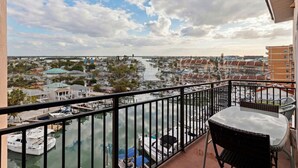 A balcony with a view of a marina, boats, and a distant shoreline. - Lovely Water View Condo | Top Floor | Steps to Beach (Madeira Beach)