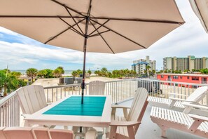 A balcony with a table and chairs, an umbrella, and a view of the beach and buildings.