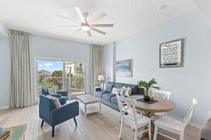 Una sala moderna con ventilador de techo, un juego de sofá, una mesa de comedor con sillas y vistas al exterior.