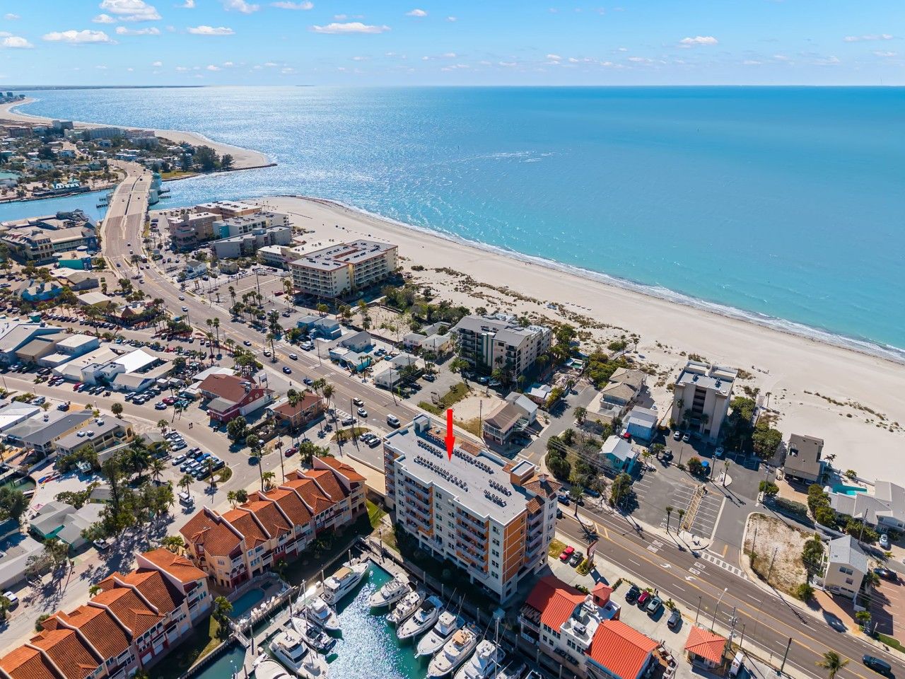 An aerial view of a coastal town with a marina, buildings, and a beach.
