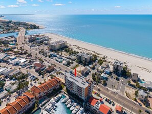 An aerial view of a coastal town with a marina, buildings, and a beach.