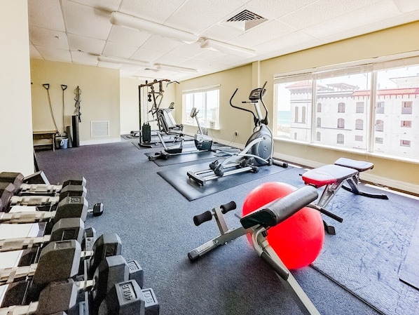 A gym with exercise equipment, a red exercise ball, and windows with a view of buildings. - Coastal Retreat in Madeira Beach/Johns Pass (Madeira Beach)