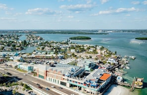An aerial view of a coastal town with a marina, buildings, and a road. - Coastal Retreat in Madeira Beach/Johns Pass (Madeira Beach)