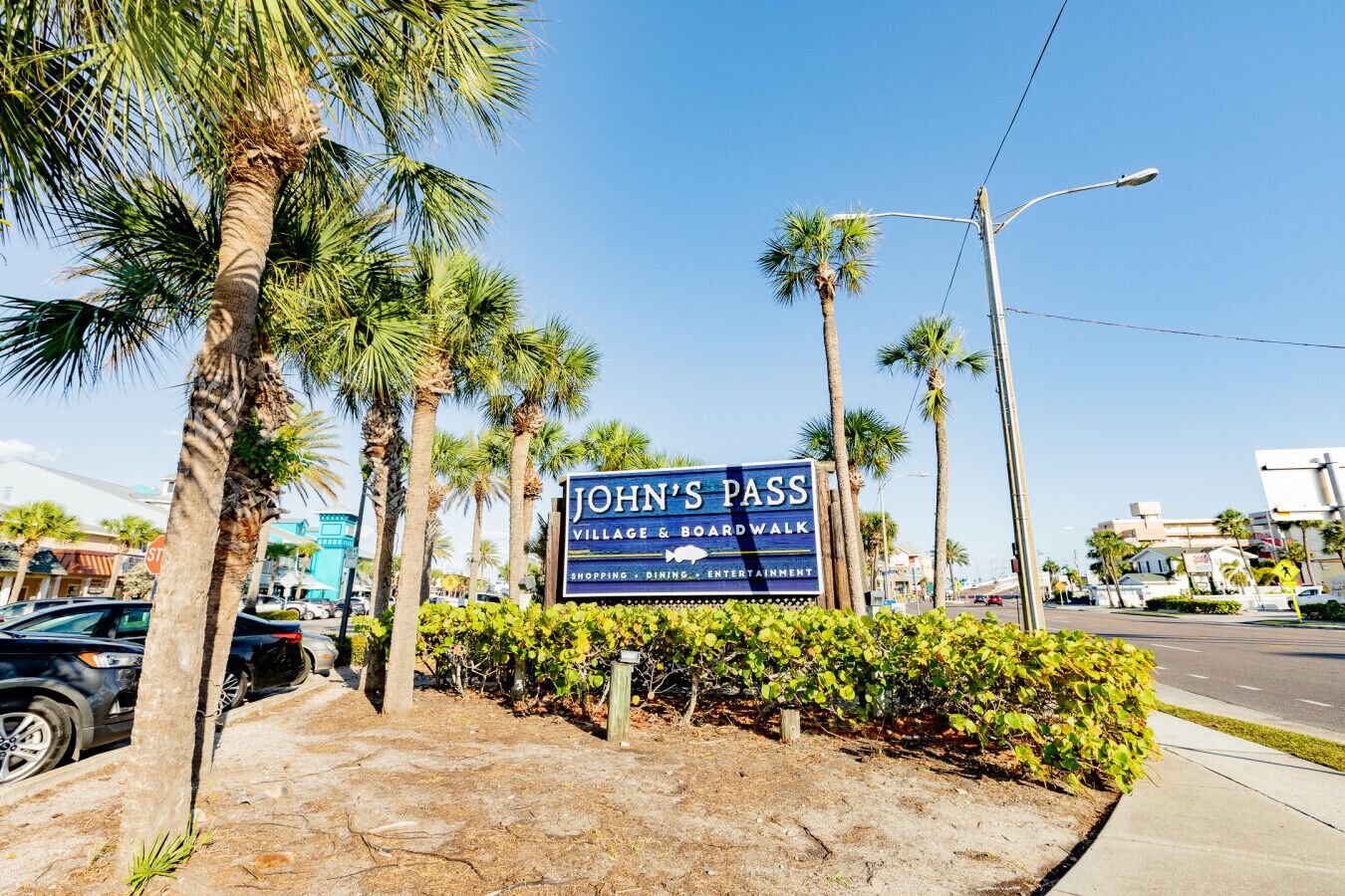 A sign for 'John's Pass Village & Boardwalk' with a clear view of the surrounding palm trees and a street.