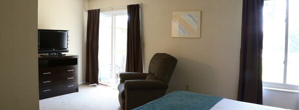 Ein Hotelzimmer mit Bett, Fernseher auf einer Kommode, einem Sessel und einem Fenster mit Vorhängen.