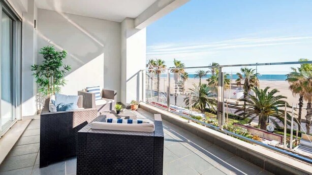 A balcony with a view of the beach, furnished with wicker furniture and potted plants. - Modern flat with sea views in Valencia. (Valencia)