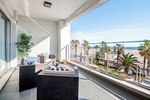 Een balkon met uitzicht op het strand, ingericht met rieten meubels en plantenpotten.