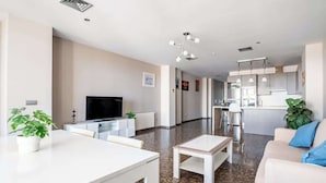 A modern living room with a TV, white furniture, a kitchen in the background, and a dining area. - Modern flat with sea views in Valencia. (Valencia)