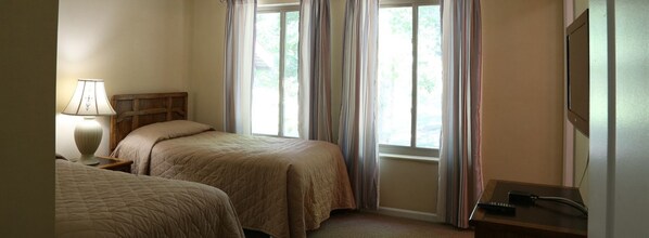 Habitación de hotel con dos camas, una mesita de noche con lámpara, un escritorio con control remoto y una ventana con cortinas.