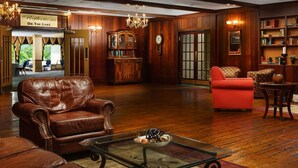 Una habitación acogedora con paneles de madera, sillones de cuero, una chimenea y una estantería llena de libros.