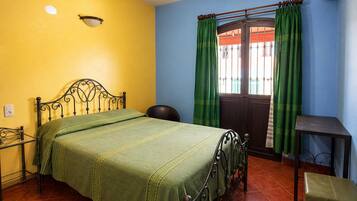 Una habitación con cama, una silla, una mesita y una ventana con cortinas.