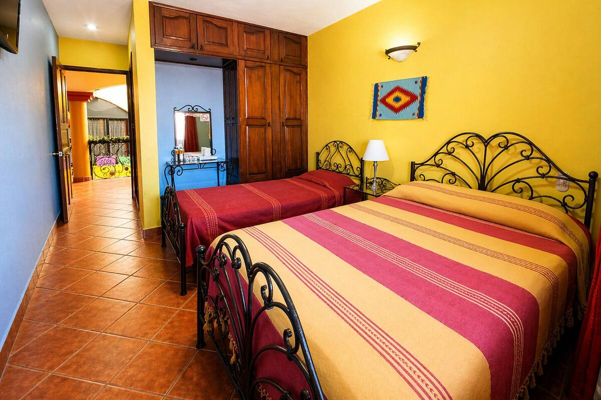 Una habitación con dos camas, armarios de madera, un espejo y una pared amarilla.