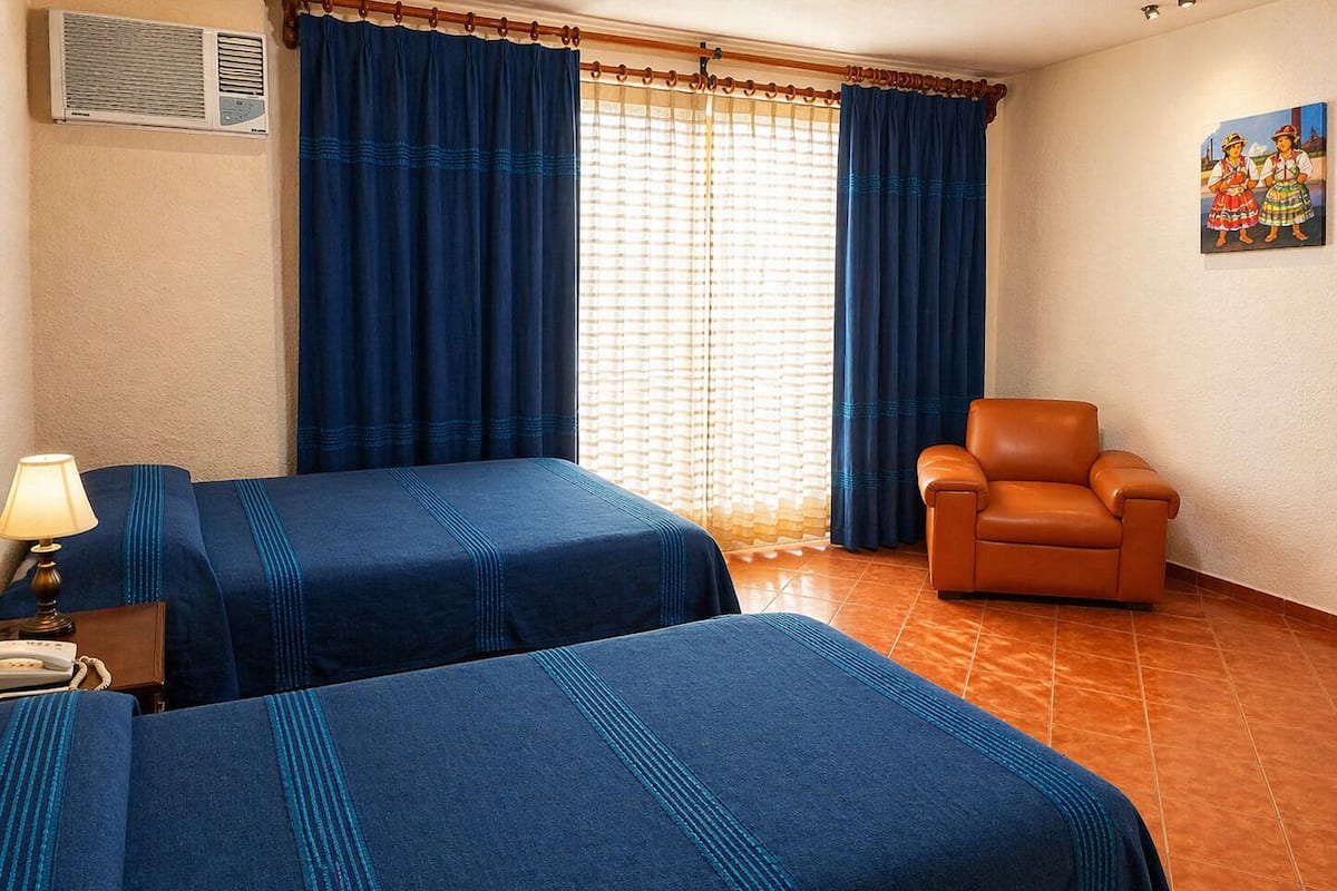 Una habitación de hotel con dos camas, una silla, una lámpara y un cuadro en la pared.
