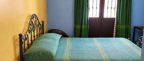 Una stanza con un letto, un tavolino con il telefono e una finestra con tende.