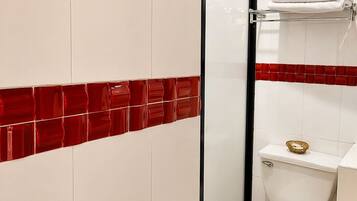 Une salle de bain avec des carreaux de céramique blancs, un mur d’accent recouvert de carreaux rouges, des toilettes blanches et un porte-serviettes.