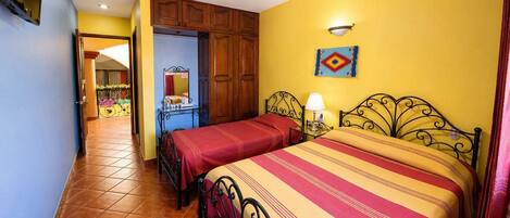 A bedroom with two beds, a wooden wardrobe, a small table with a lamp, and a ceiling fan.