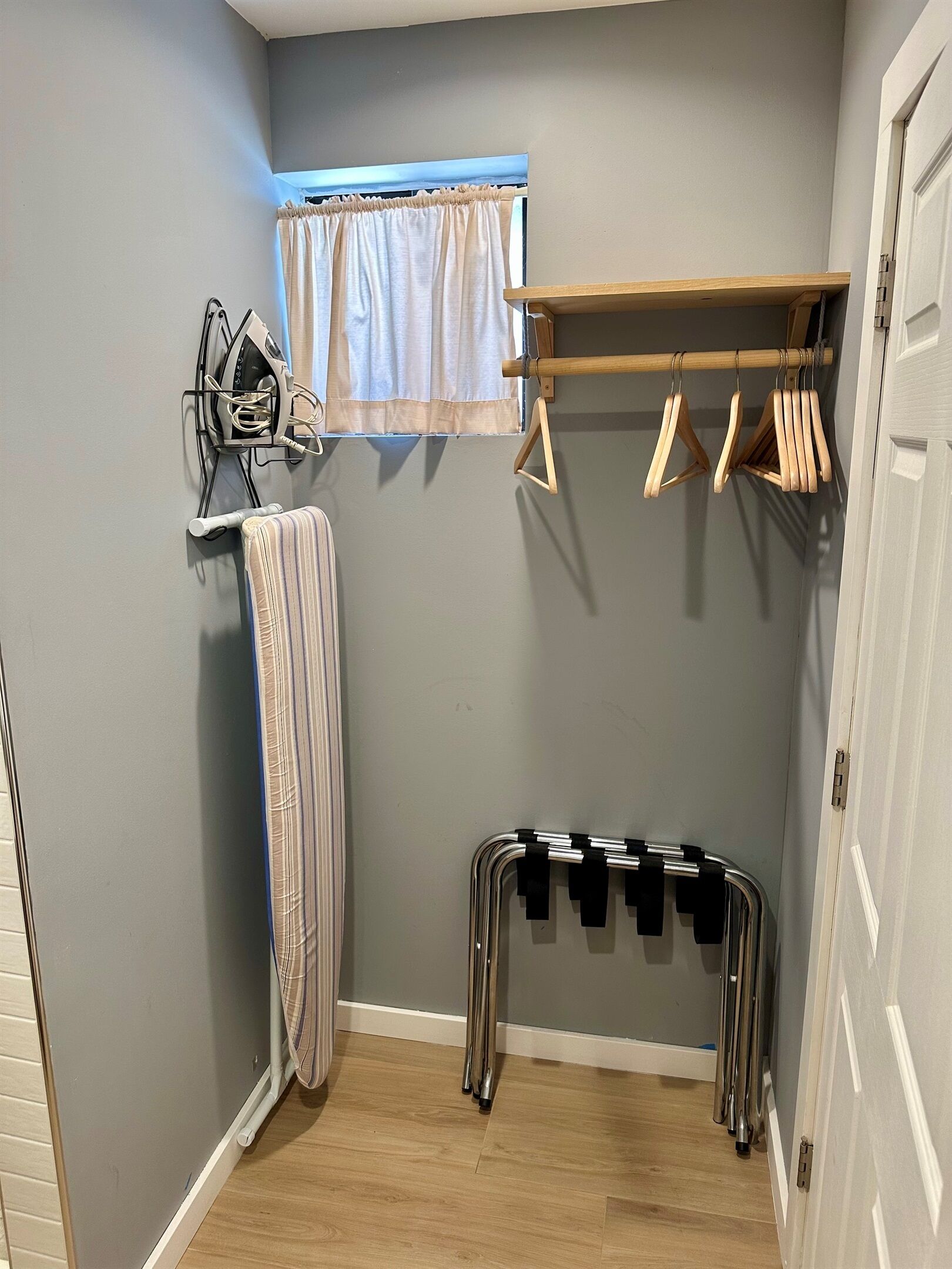 A laundry area with a drying rack, ironing board, and wooden hangers on a wall.