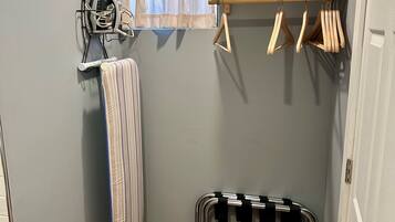 A laundry area with a drying rack, ironing board, and wooden hangers on a wall.