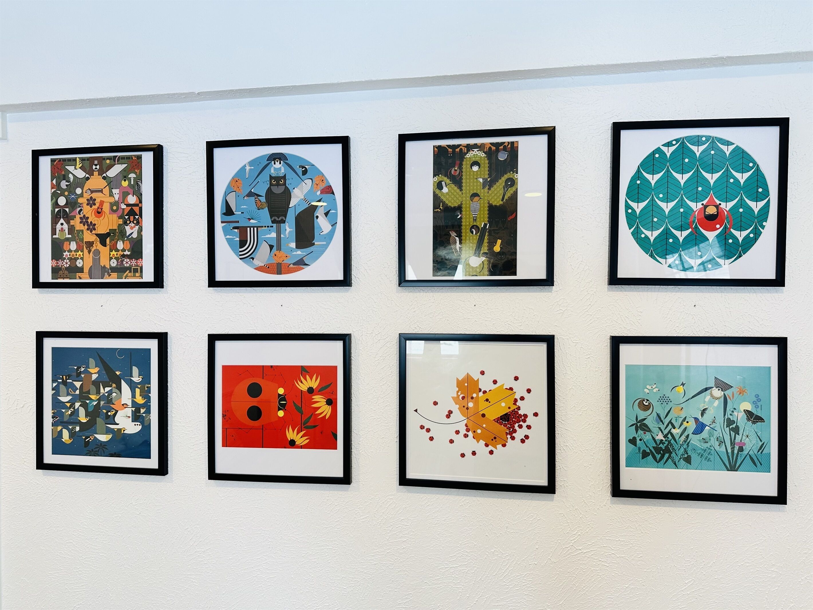Acht gerahmte Kunstwerke an einer Wand.