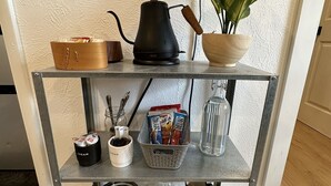 Ein Metallregal mit einer Kaffeemaschine, einer Topfpflanze, einem Korb und Küchenutensilien.