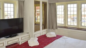 A hotel room with a large flat-screen TV, a bed with red bedding, a mirror, and windows with curtains. - 4 bedroom accommodation in Whitby (Whitby)